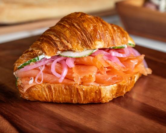 Croissant sandwich with salmon and pickled onions on a wooden surface