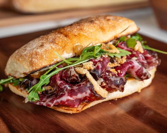Sandwich with arugula and red meat on a wooden cutting board