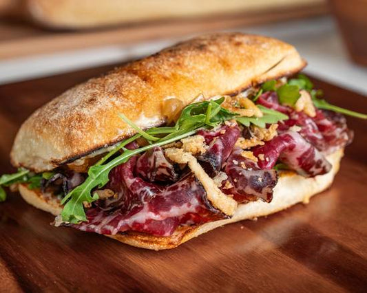Sandwich with arugula and red meat on a wooden cutting board