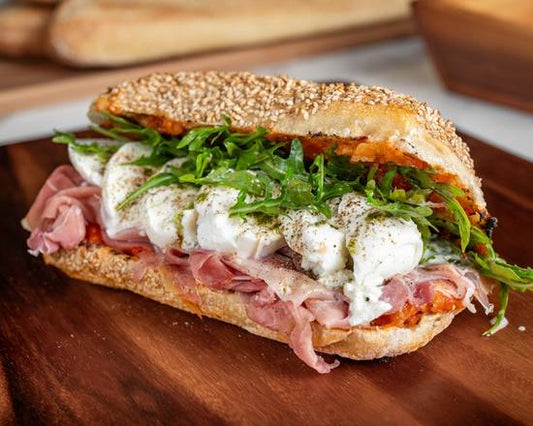 Sandwich with ham, arugula, and a white sauce on a wooden cutting board.