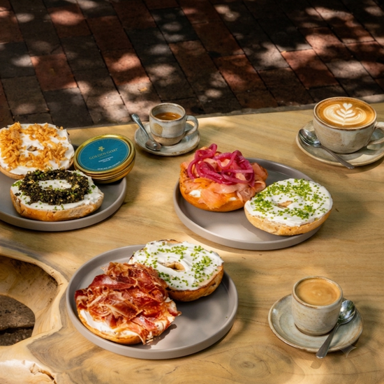 Assorted bagels with different toppings and coffee cups on a wooden table.