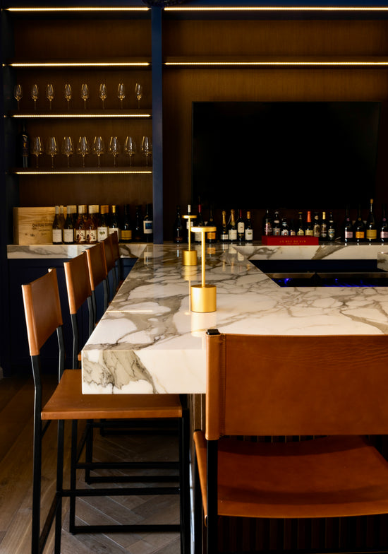 Modern bar setting with marble countertop, chairs, and shelves with bottles.