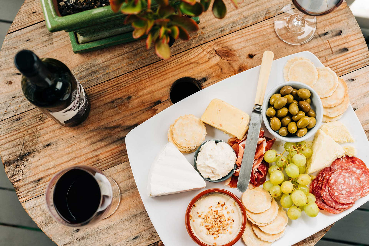Tablescape of cured meats, cheeses, grapes and hummus. 